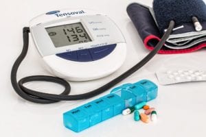 Electronic blood pressure cuff with a blue pill box with pills that are blue orange and blue and white